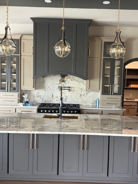 Modern kitchen with gray cabinetry, granite countertops, black gas range, and three hanging pendant lights with glass globes