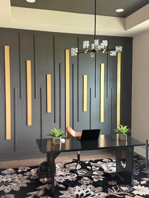 Modern office space with dark desk, laptop, green plants, pendant lighting, and dark paneled wall with gold accents