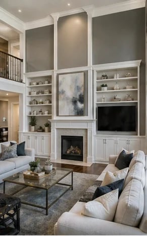Modern living room with two-story fireplace feature wall, built-in shelving, mounted TV, cream seating, and geometric coffee table